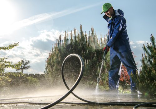 Garden Washing Maintenance. Caucasian Worker in His 30s with Pressure Washer Cleaning Brick Paths.